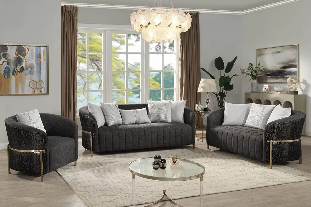 A charcoal curved channel-tufted sofa set with gold-tone bases and white scatter cushions in a bright living room.