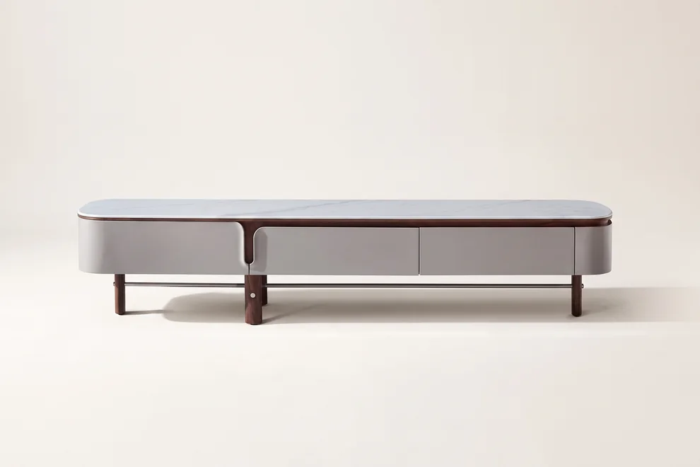 Long contemporary side cabinet with a smooth top, rounded corners and slim raised legs standing against a wall.